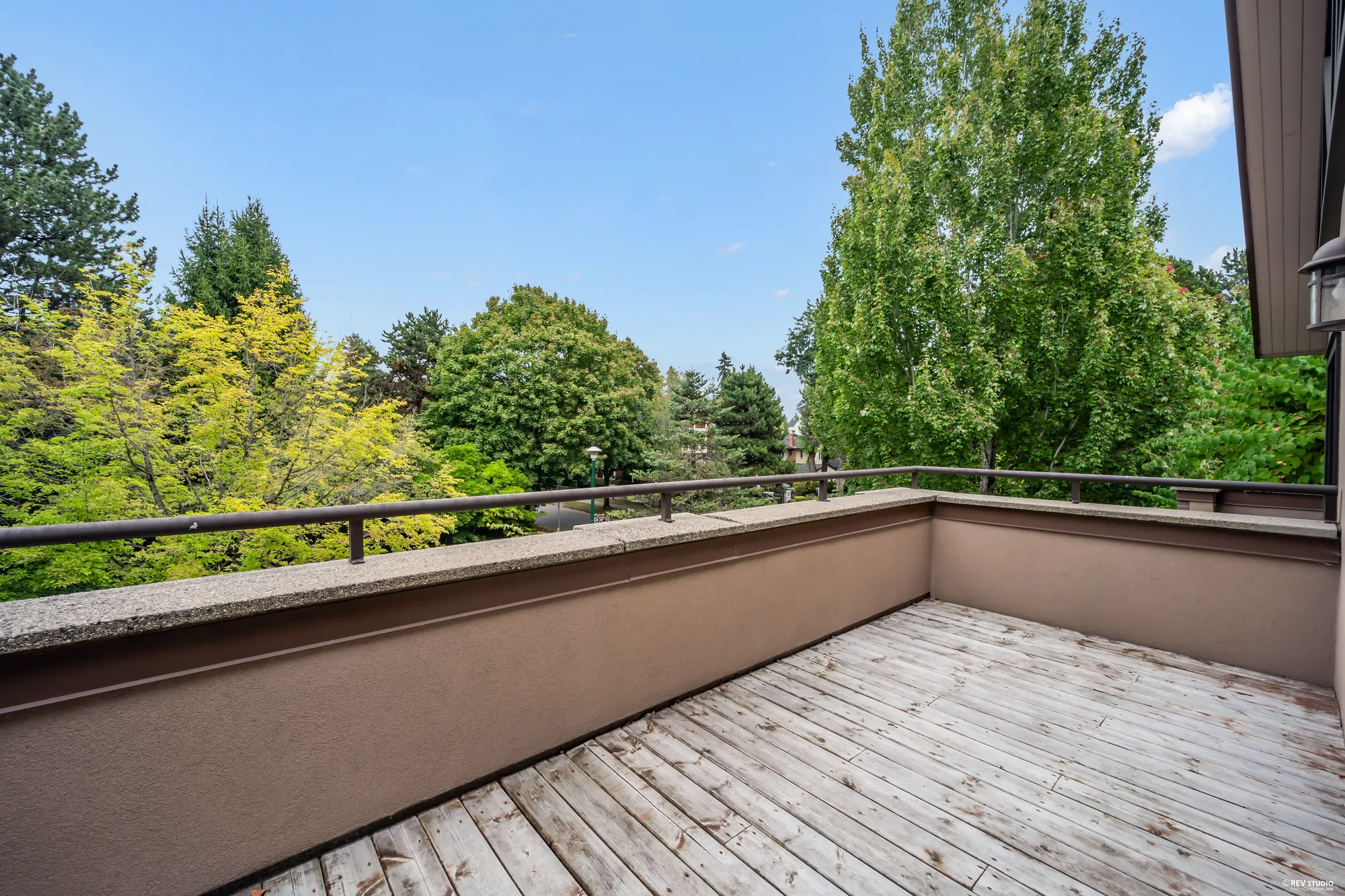 The upper balcony over the entry: a weathered wood deck behind a stucco parapet, the trees beyond