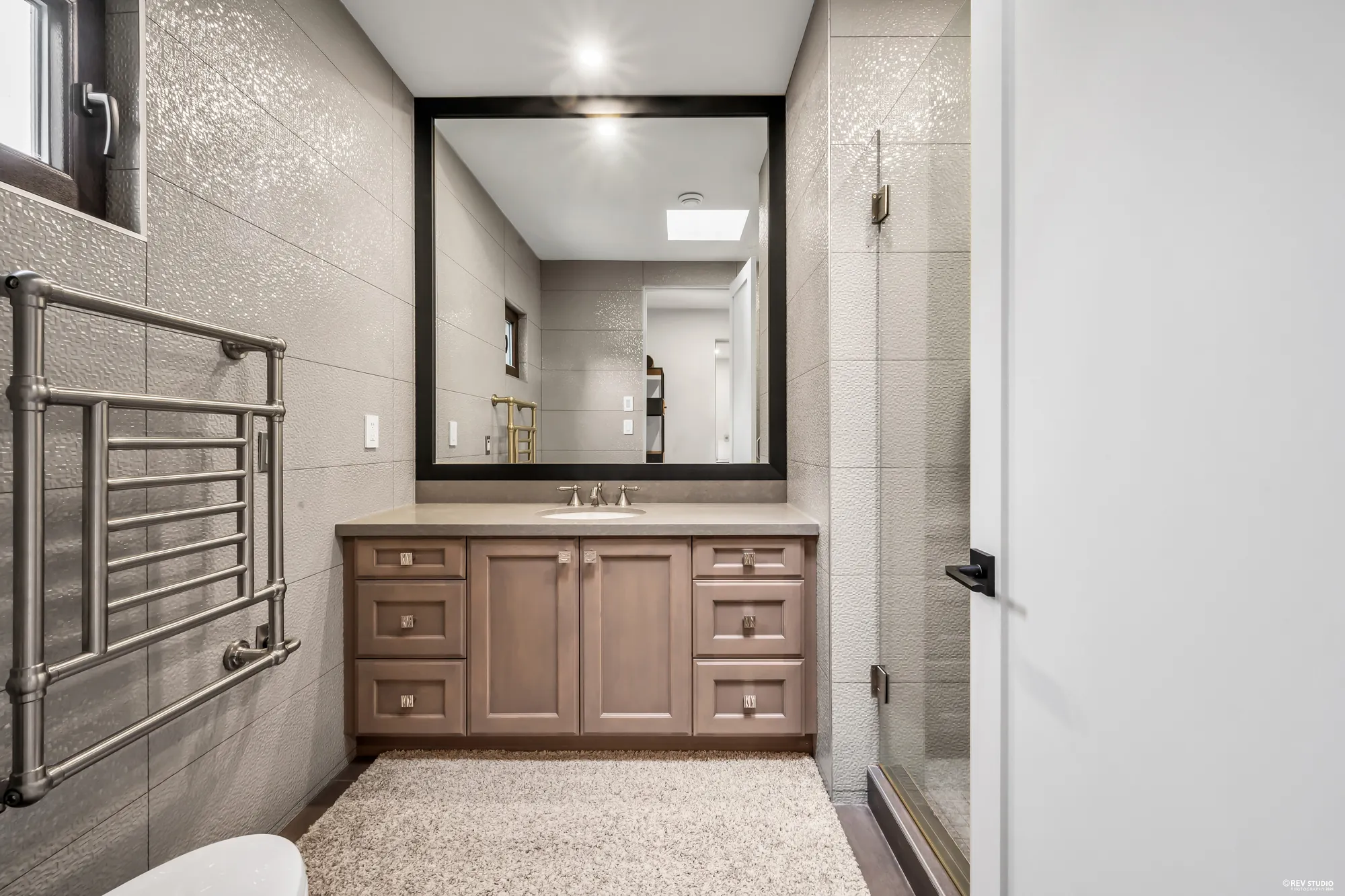 The hall bathroom: a wooden vanity under a framed mirror, grey tile, the shower beyond