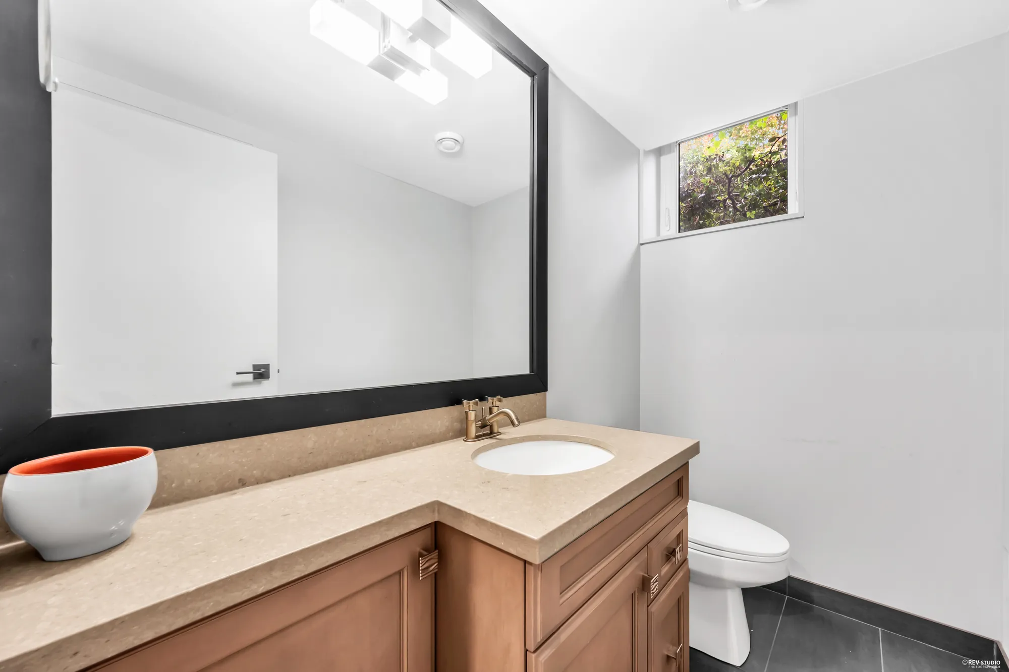 A bathroom vanity and toilet under a small window, a bowl on the counter