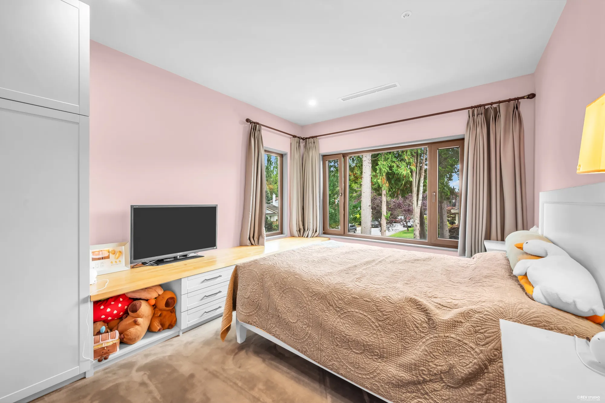 A bedroom in pink with a corner window, a desk under it