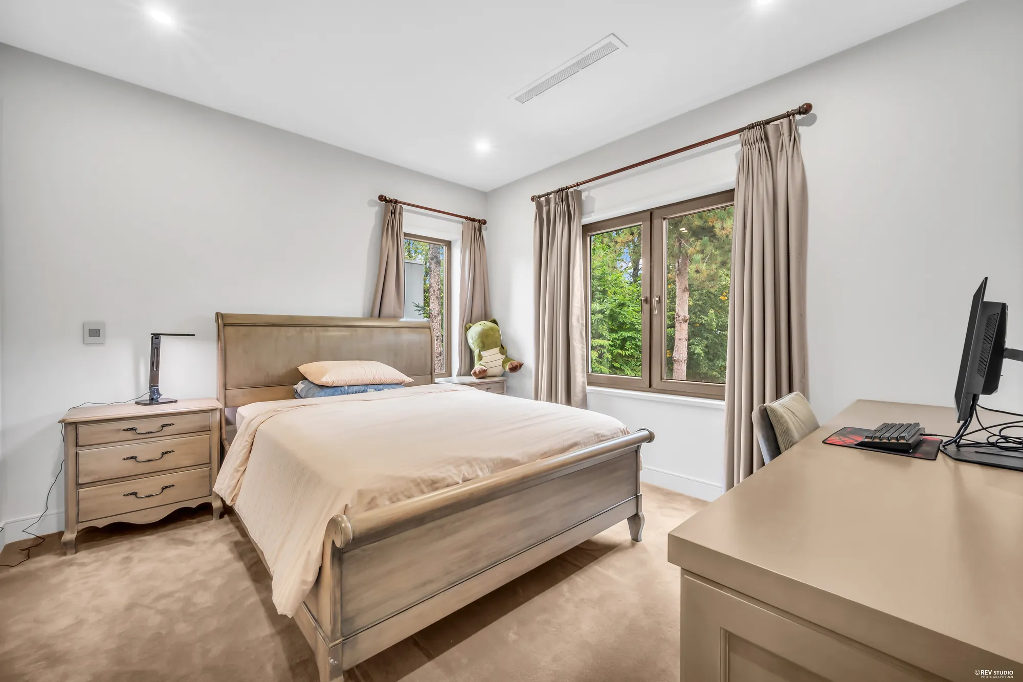 A bedroom with a desk at the window, a bed and a dresser