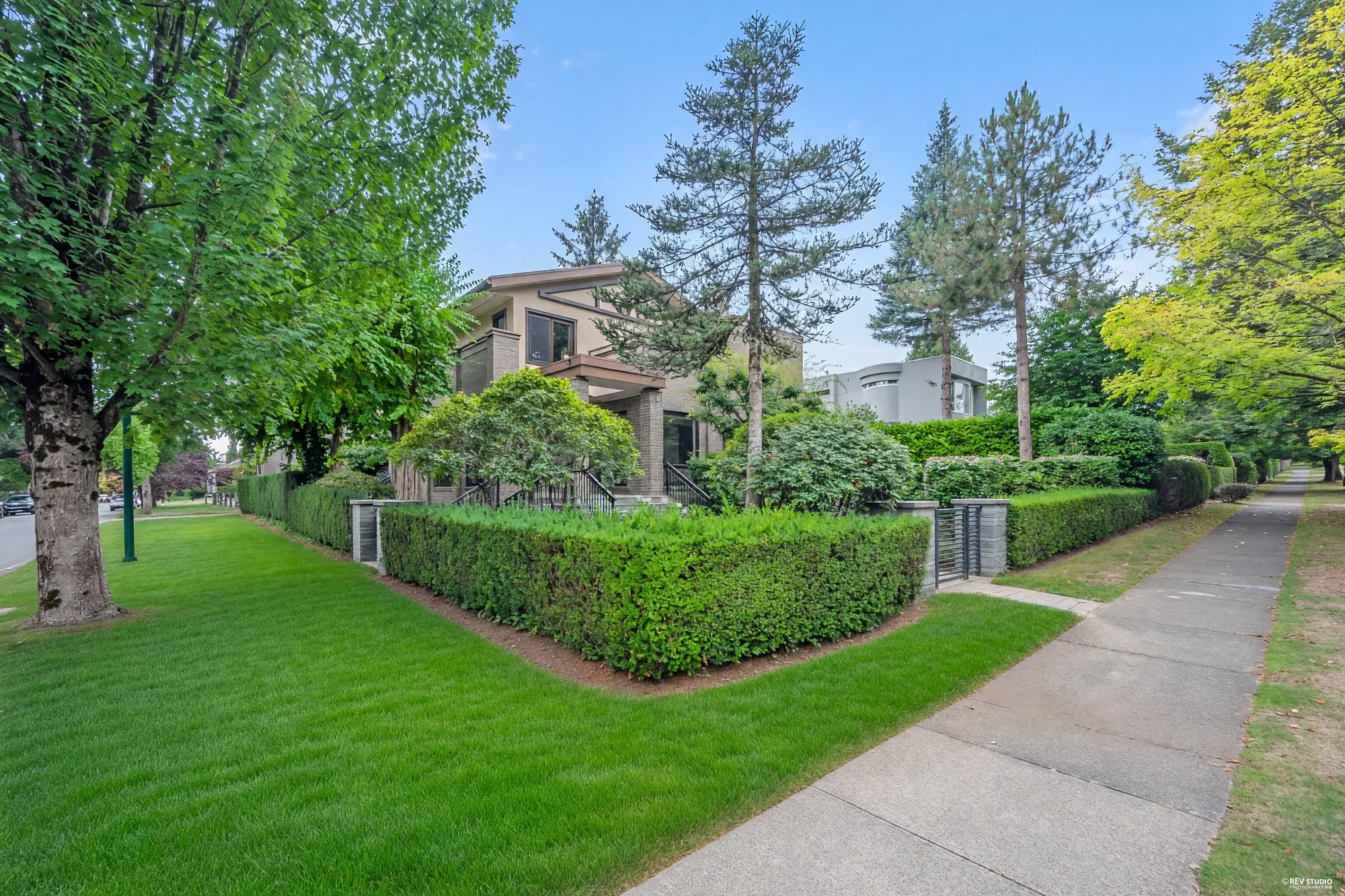 The corner of the lot: the clipped hedge on two sides, the gate, the house behind and the boulevard lawn
