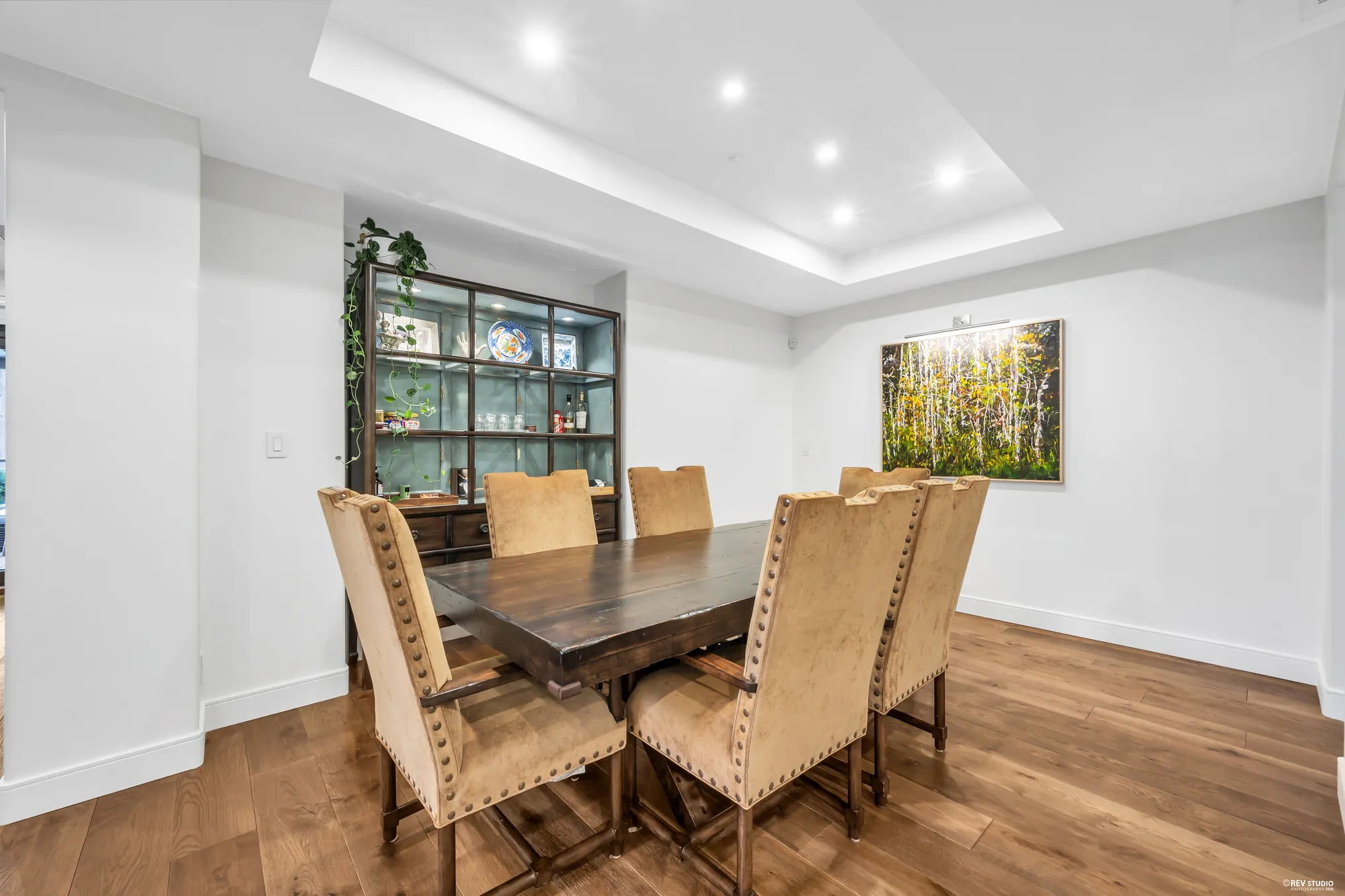 The dining room: a long dark table with upholstered chairs, a glass-fronted cabinet at the end, a painting