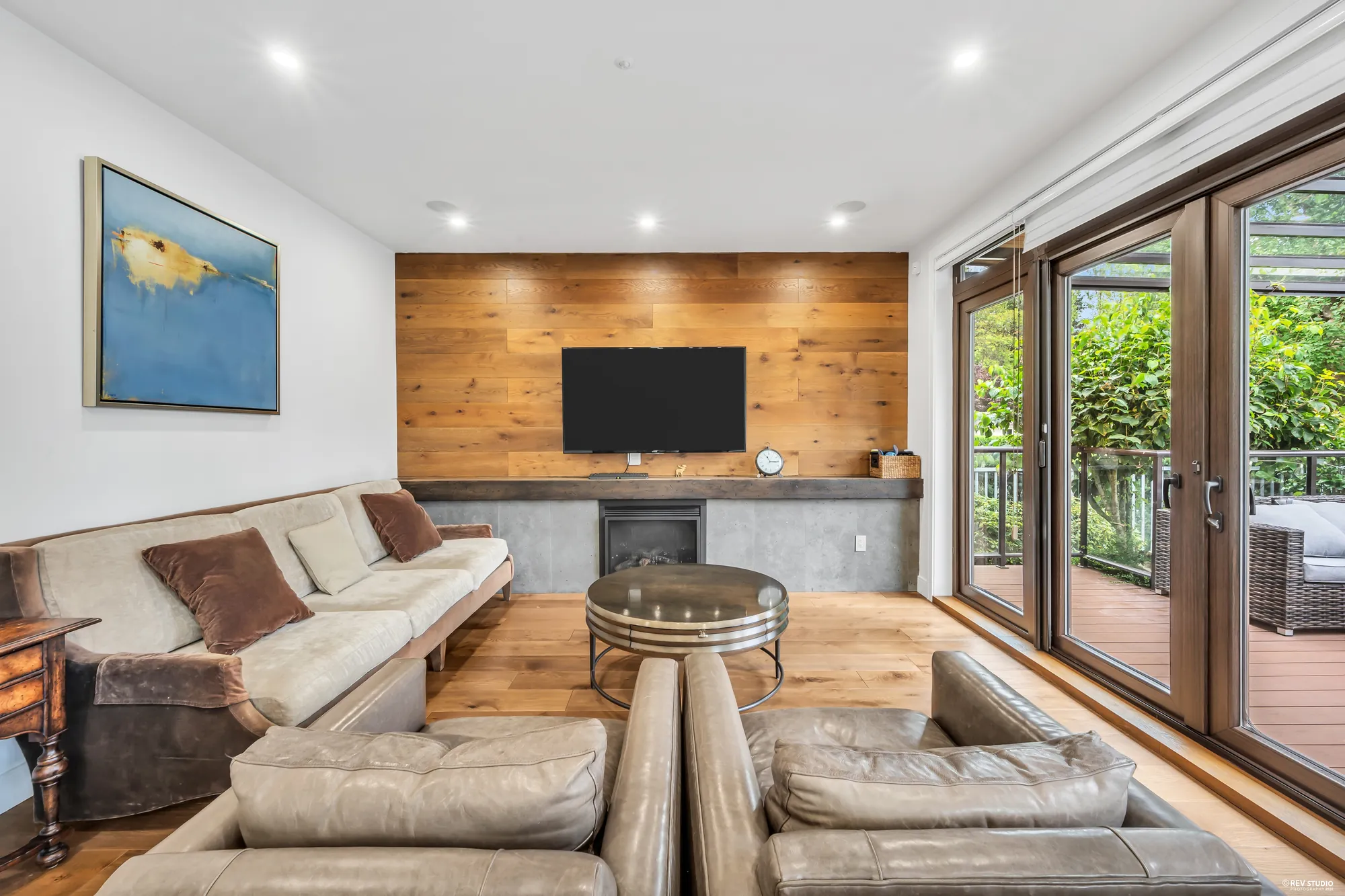 The family room: a wood-clad wall carrying the television and a fireplace, oak floors, and glass doors to the deck on the right