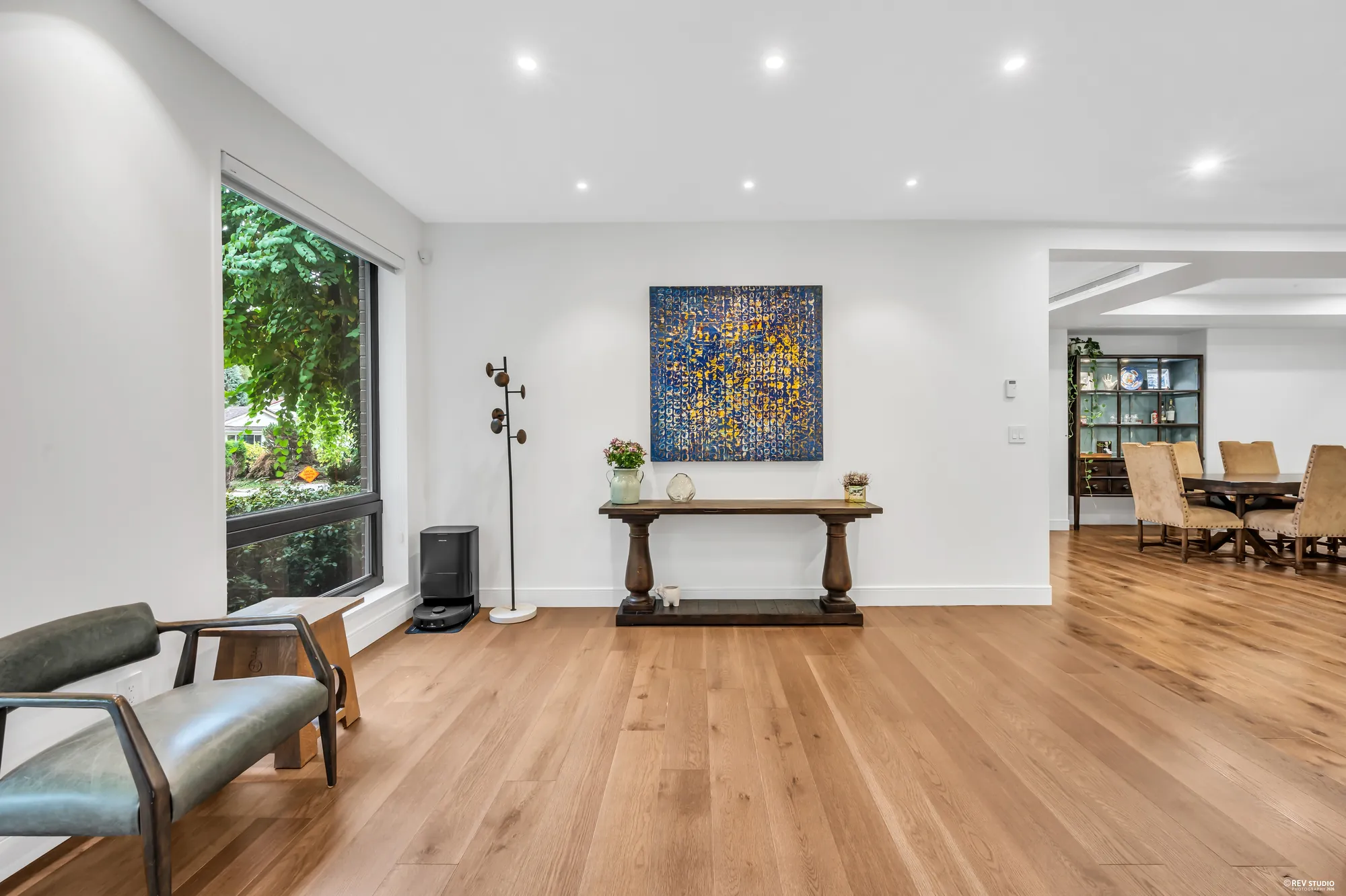 The hall with a console under a painting, the dining room beyond, an armchair by the window
