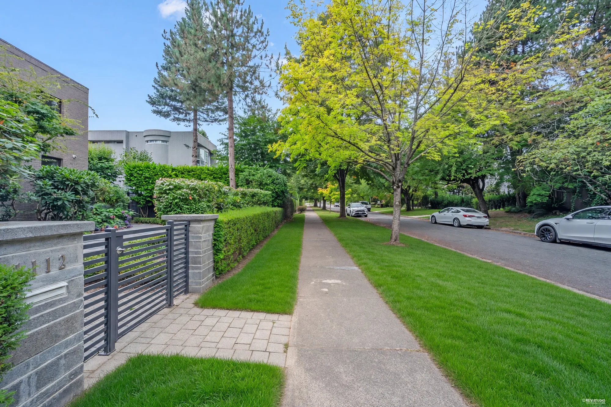 The gate in its block pillars with the number 1112, the sidewalk and the boulevard under the street trees