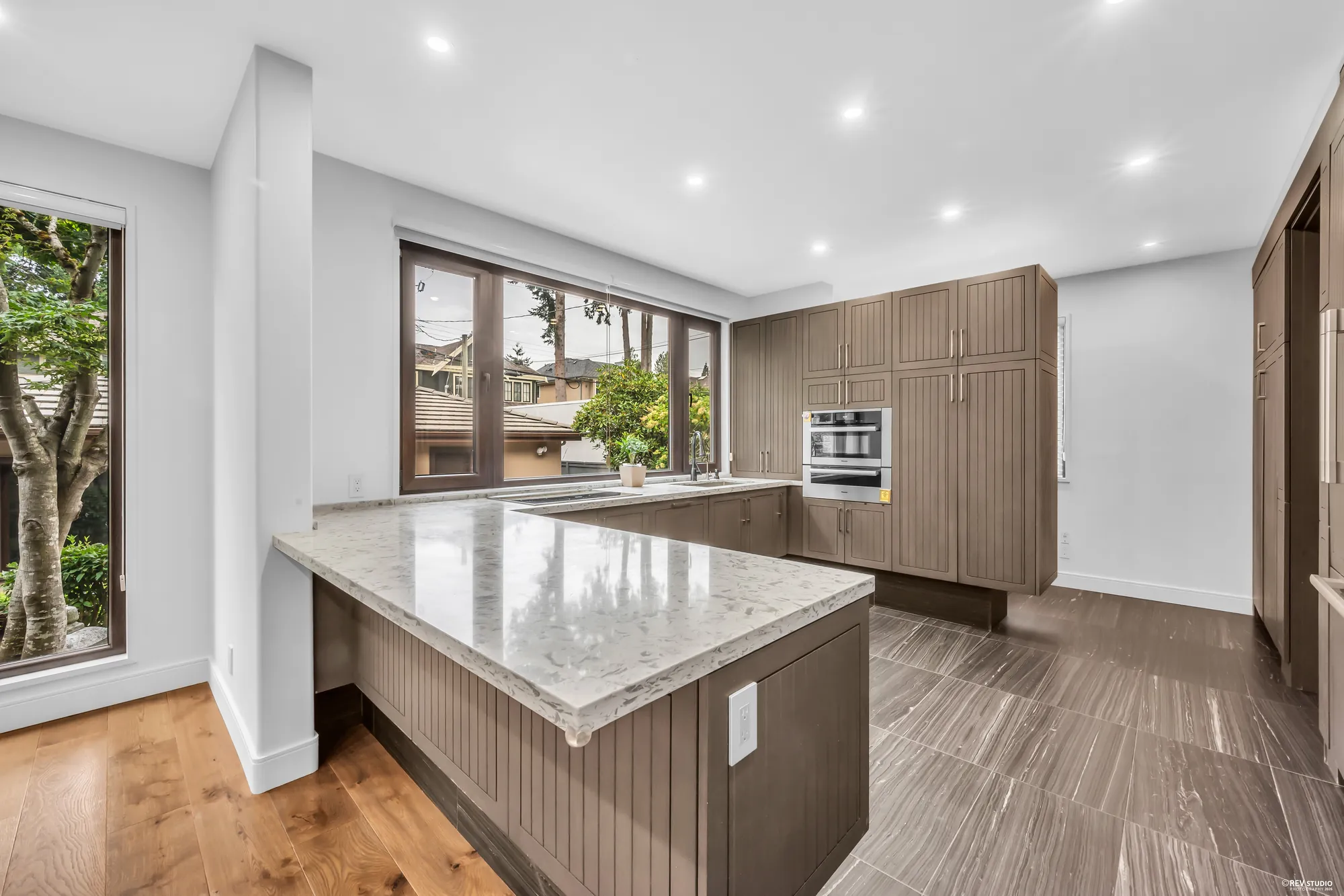 The kitchen: an island with a marbled quartz top, taupe cabinets, and windows over the counter onto the garden