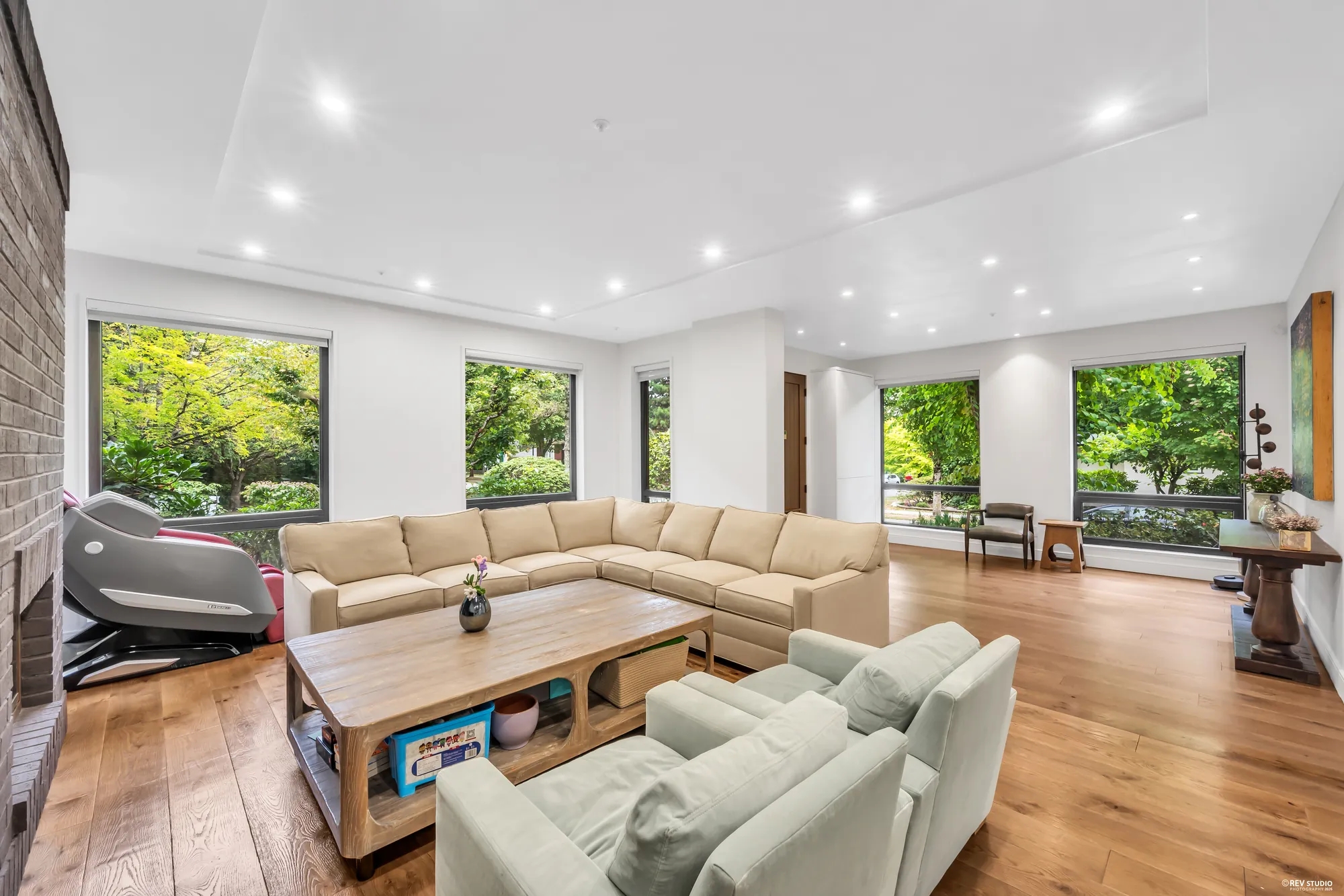 The living room: a pale sectional facing the brick fireplace, windows on two sides, oak floors