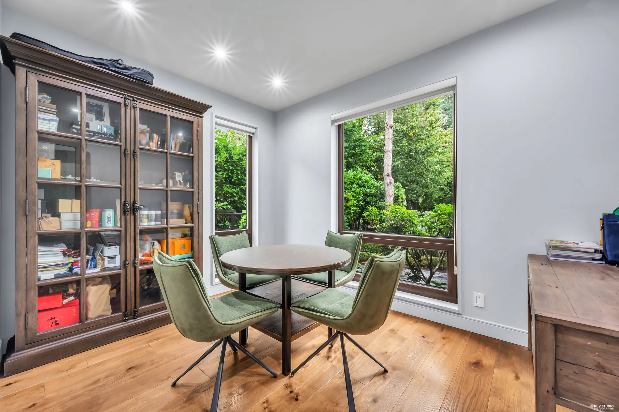 The office: a glass-fronted cabinet, a round table with green chairs, a window onto the garden