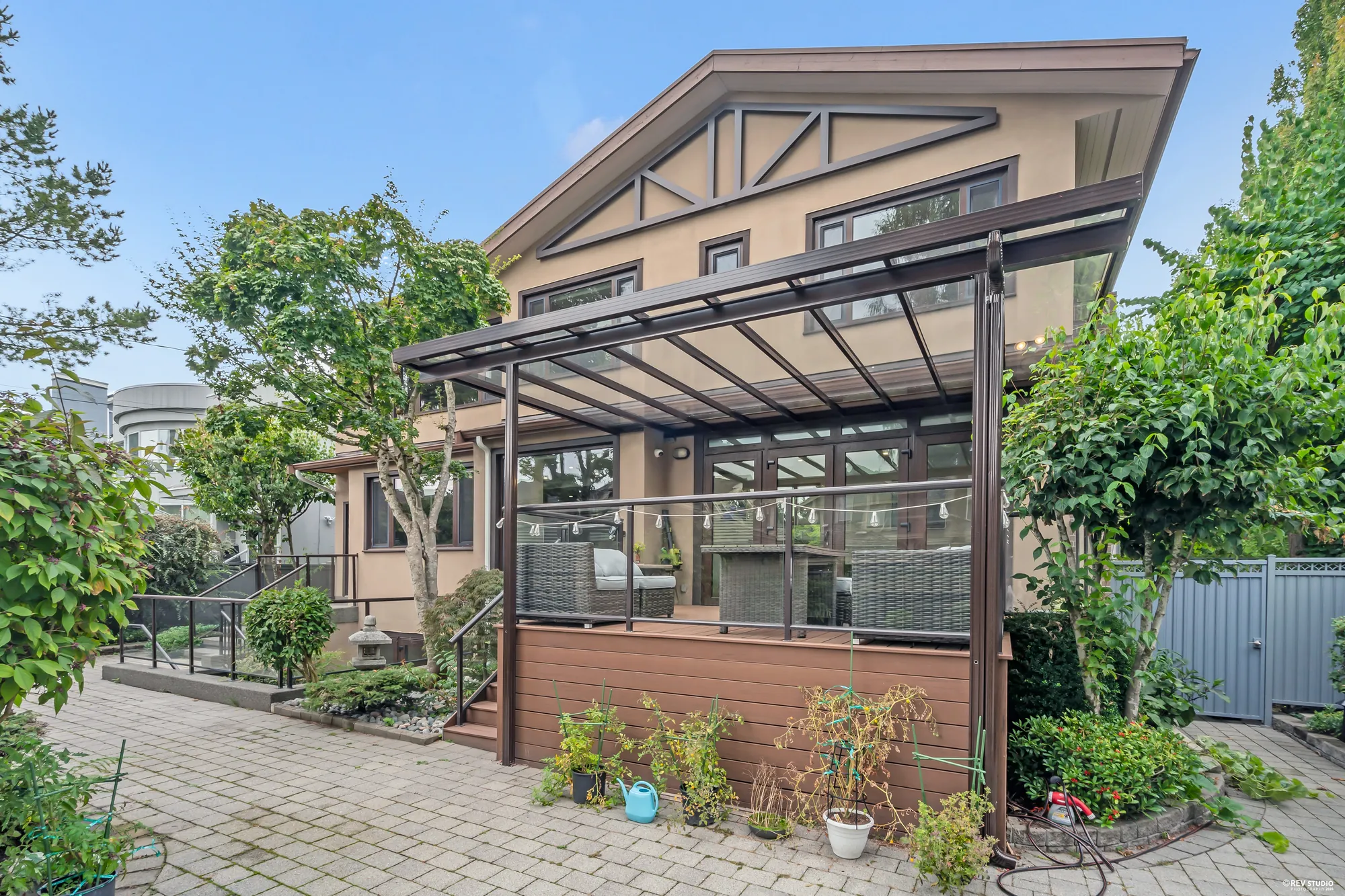 The back of the house with the glass-roofed pergola over the deck, planting along the wall and the motor court in front