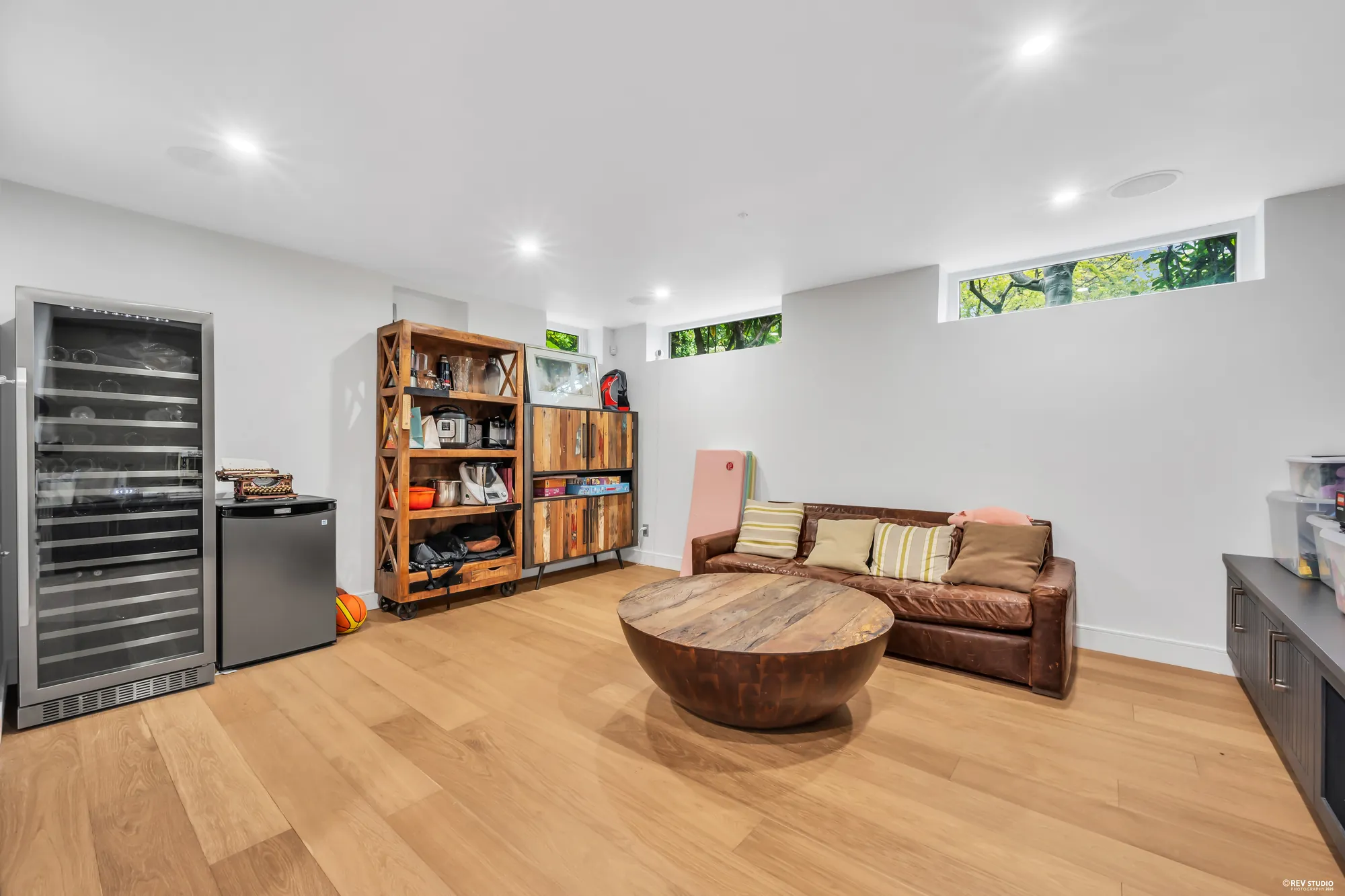 The room drawn as the theatre: a wine fridge, open shelving and a leather sofa under high windows