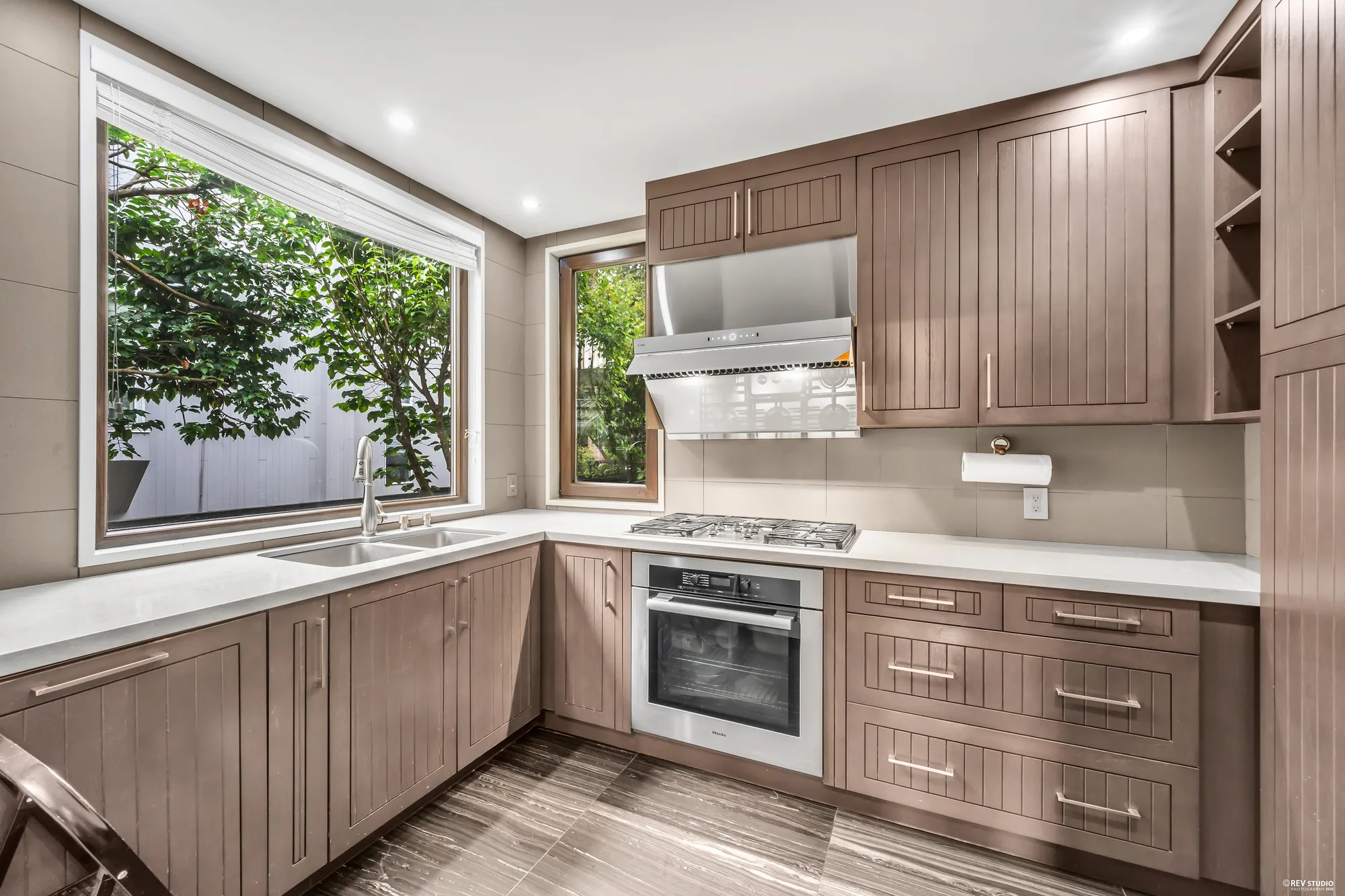 The wok kitchen: a range under its hood, a window over the sink, taupe cabinets